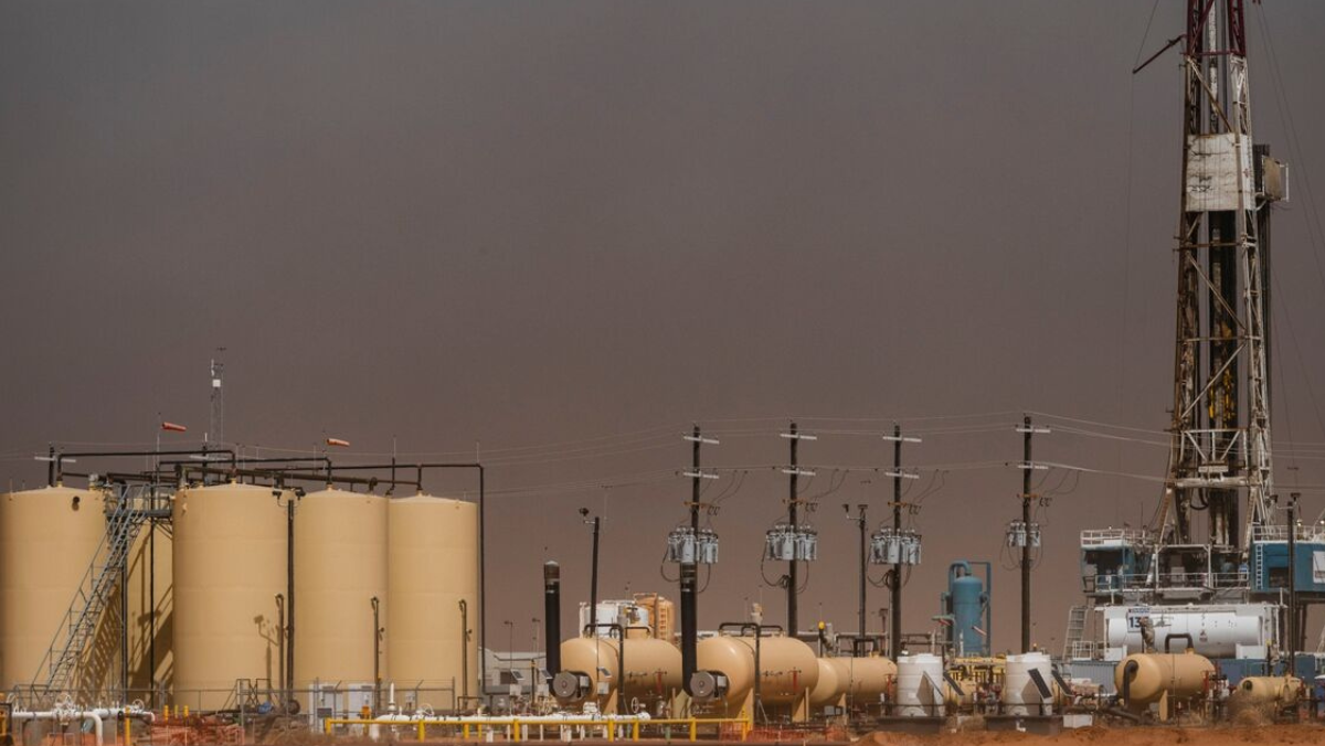 Oilfield site with storage tanks and drilling equipment under cloudy sky