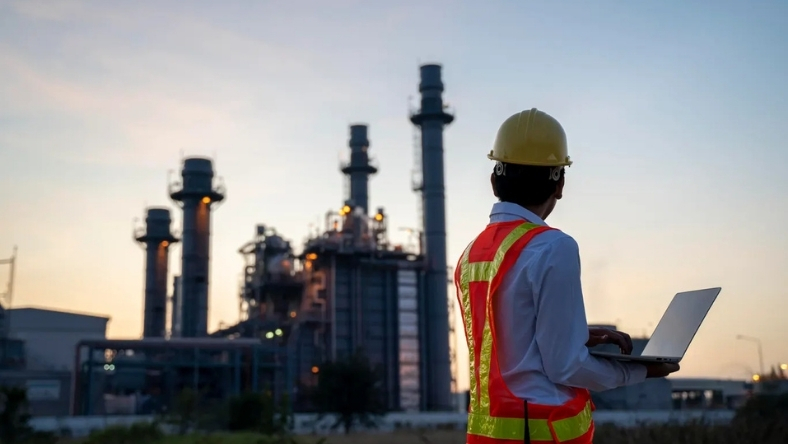 Engineer wearing safety gear uses a laptop at an industrial energy facility