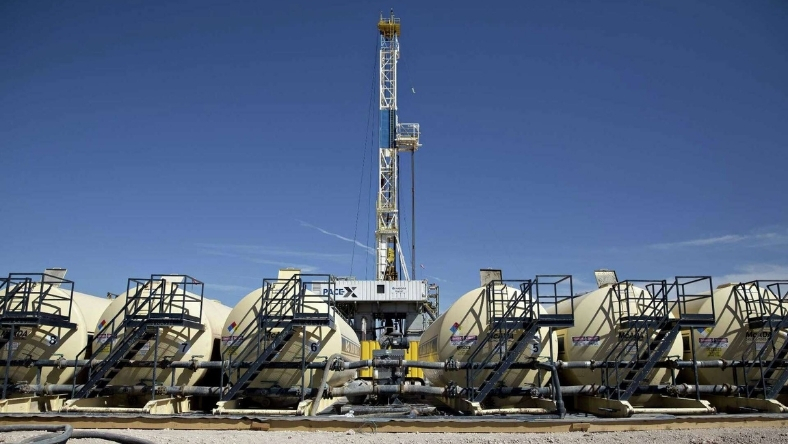 Onshore oil drilling rig with storage tanks under clear blue sky